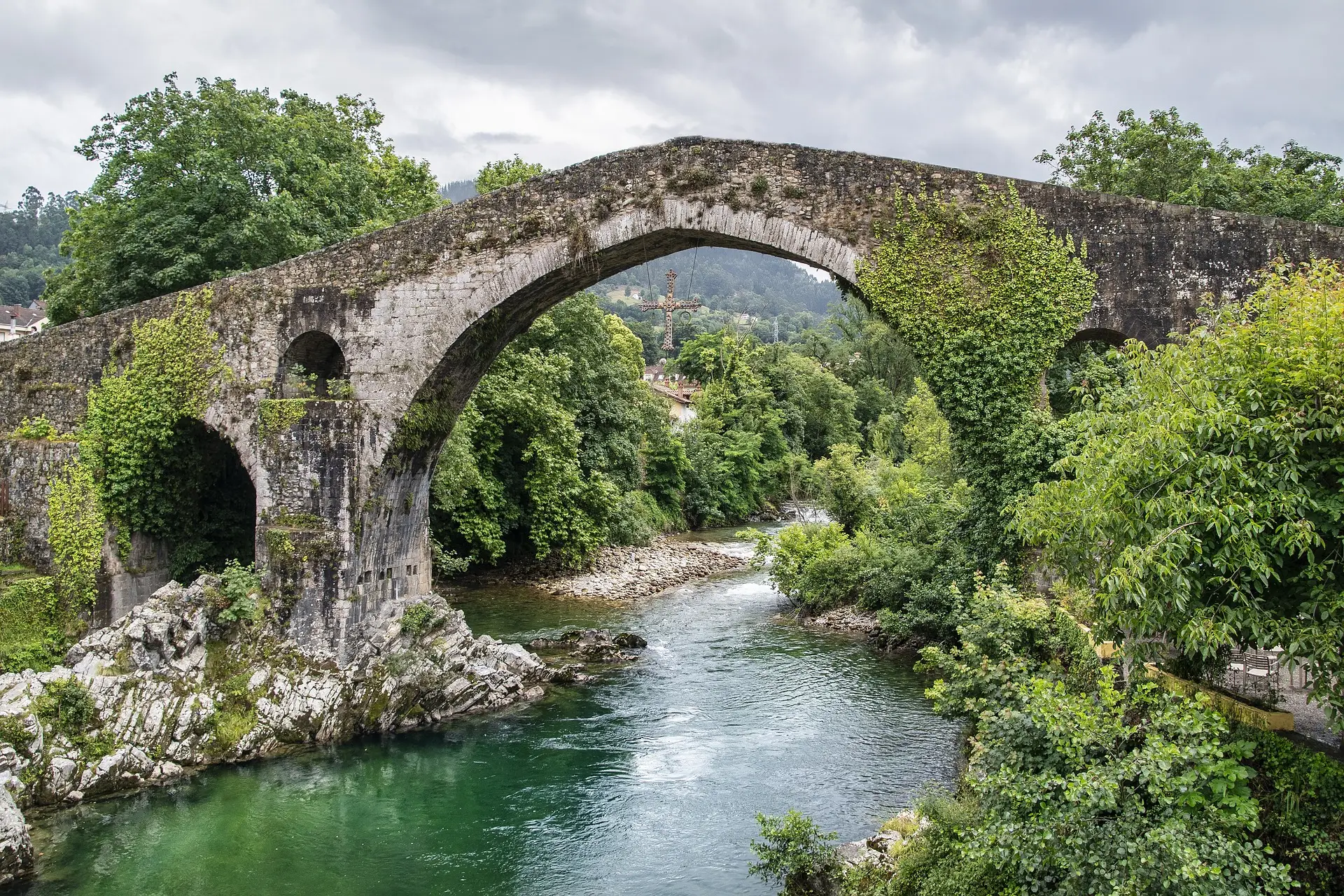 Alte Steinbrücke über einen kleineren Fluss bei leicht graueren Himmel.